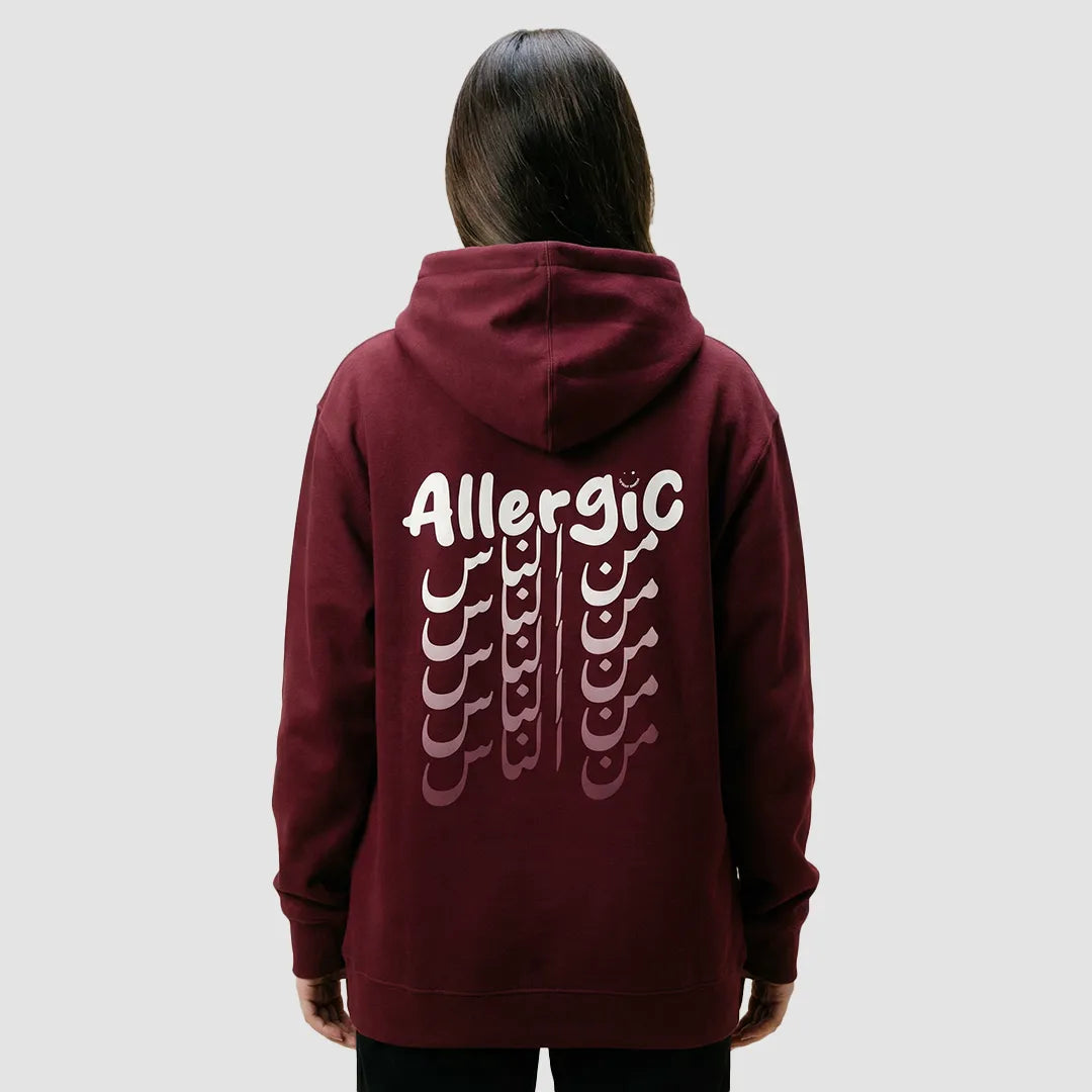 ragazza indossa felpa unisex bordeaux con cappuccio e scritta bianca in inglese ed arabo sulla schiena allergic من الناس - Totally Random®