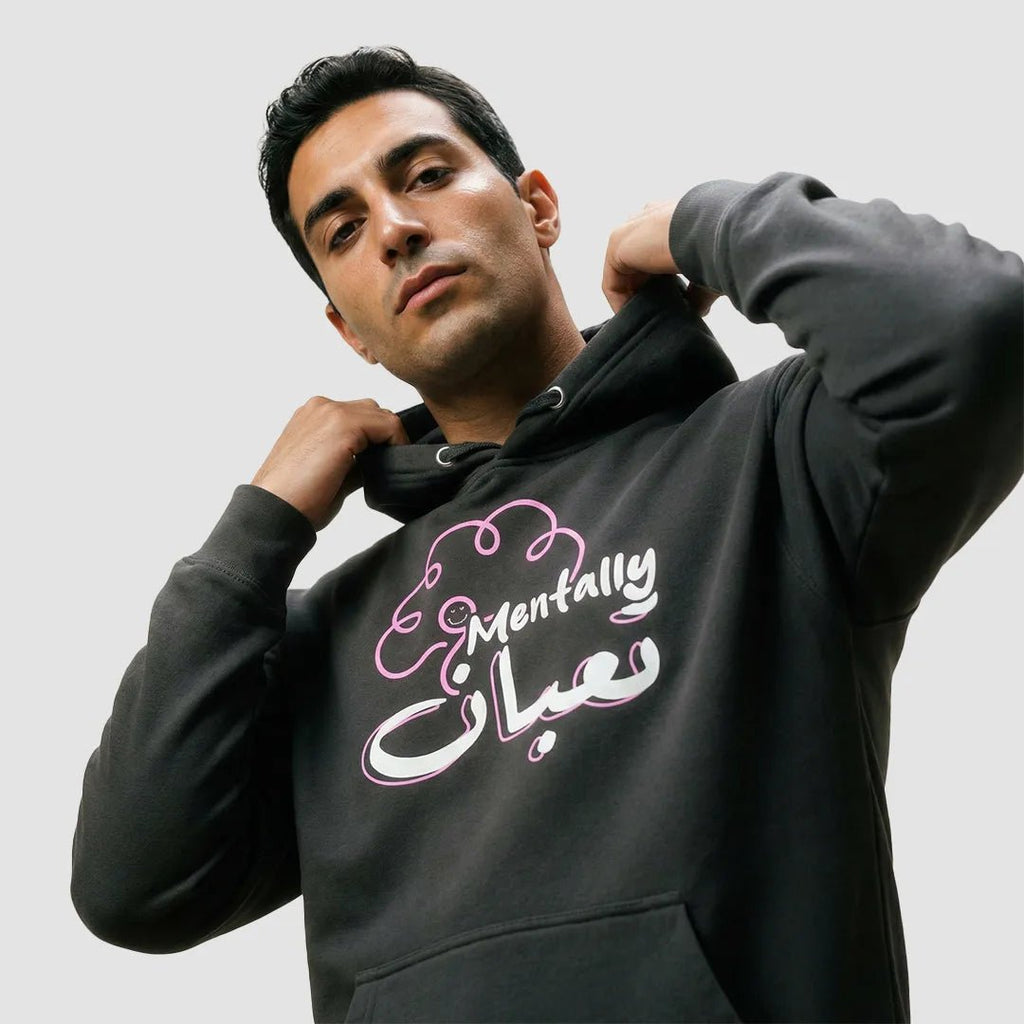 uomo indossa felpa unisex blu con cappuccio e design di un cervello rosa e scritta bianca in inglese e arabo mentally تعبان - Totally Random®