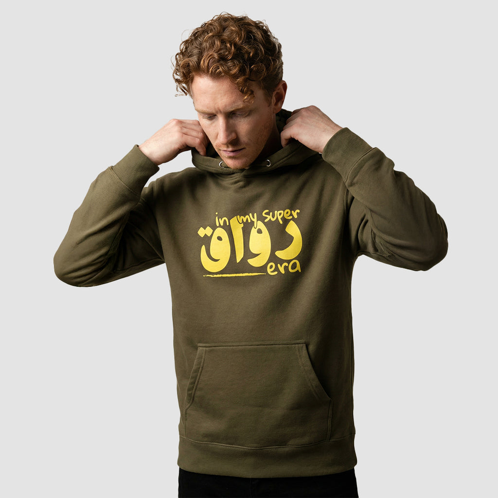 uomo indossa felpa unisex verde militare con cappuccio e scritta gialla in inglese e arabo in my super chill era - Totally Random®