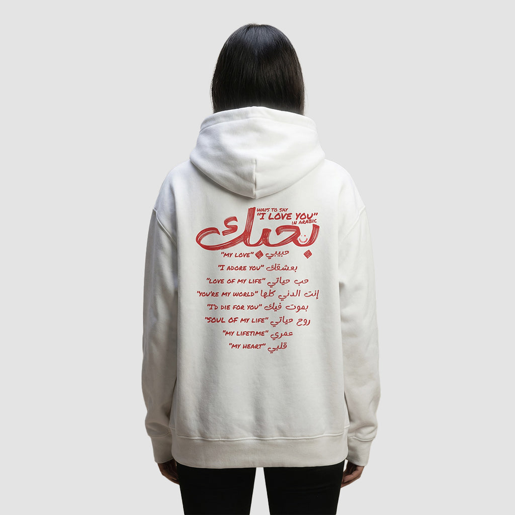 ragazza indossa felpa unisex oversize con cappuccio bianca e scritta rossa in inglese e arabo ways to say i love you in arabic - Totally Random®