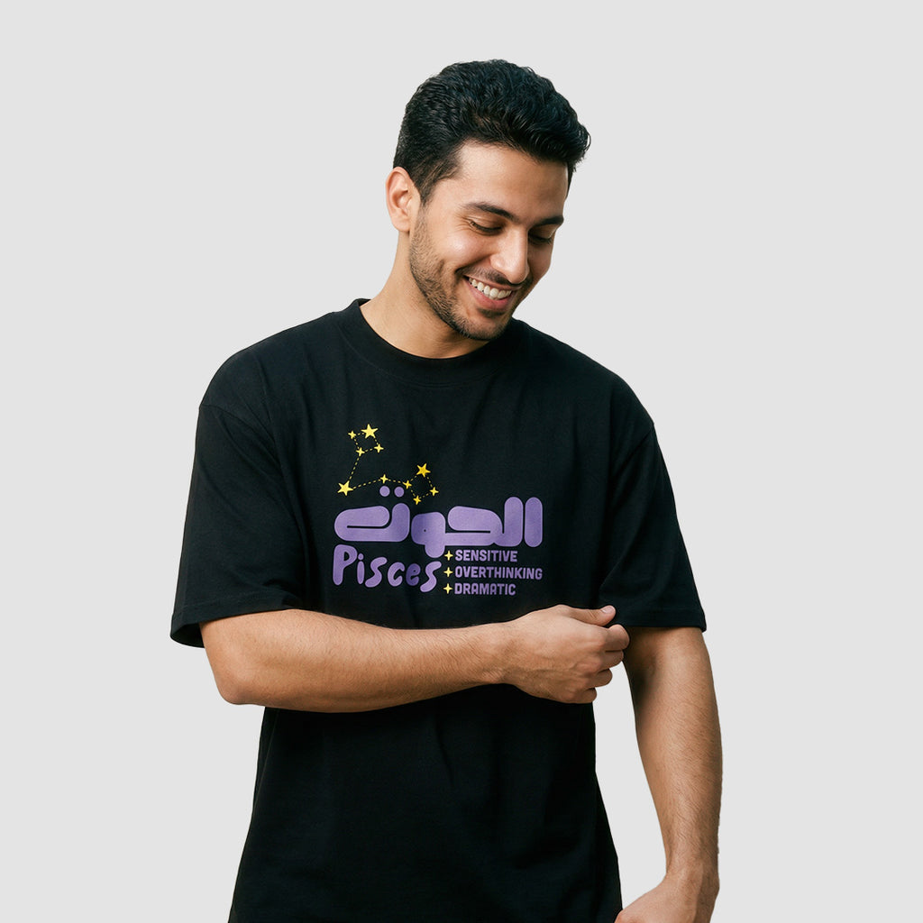 Ragazzo indossa maglietta unisex oversize nera con scritta in inglese e arabo oroscopo pisces - Totally Random®