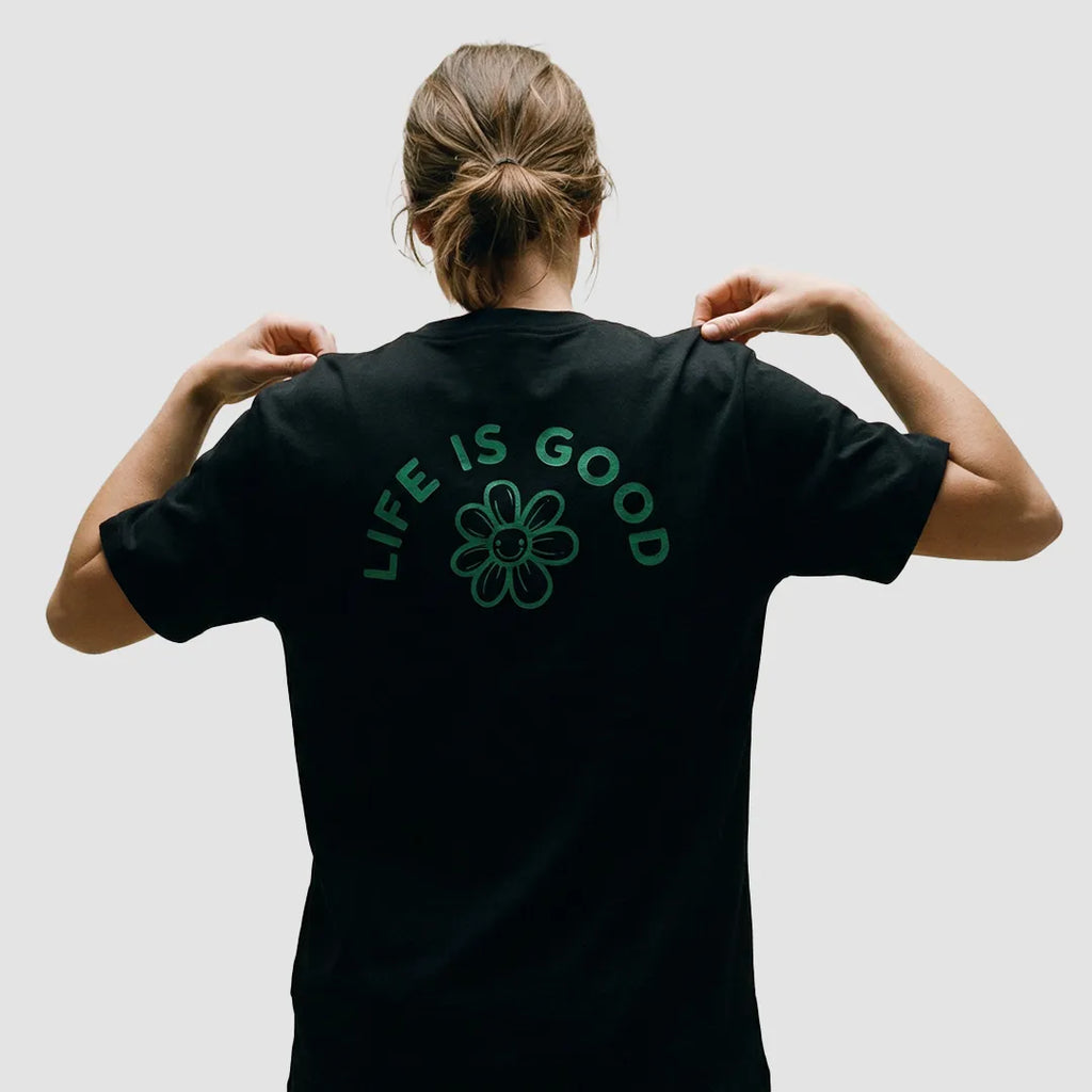 ragazza indossa maglietta unisex nera con icone di fiore e scritta verde sulla schiena Life Is Good - Totally Random®