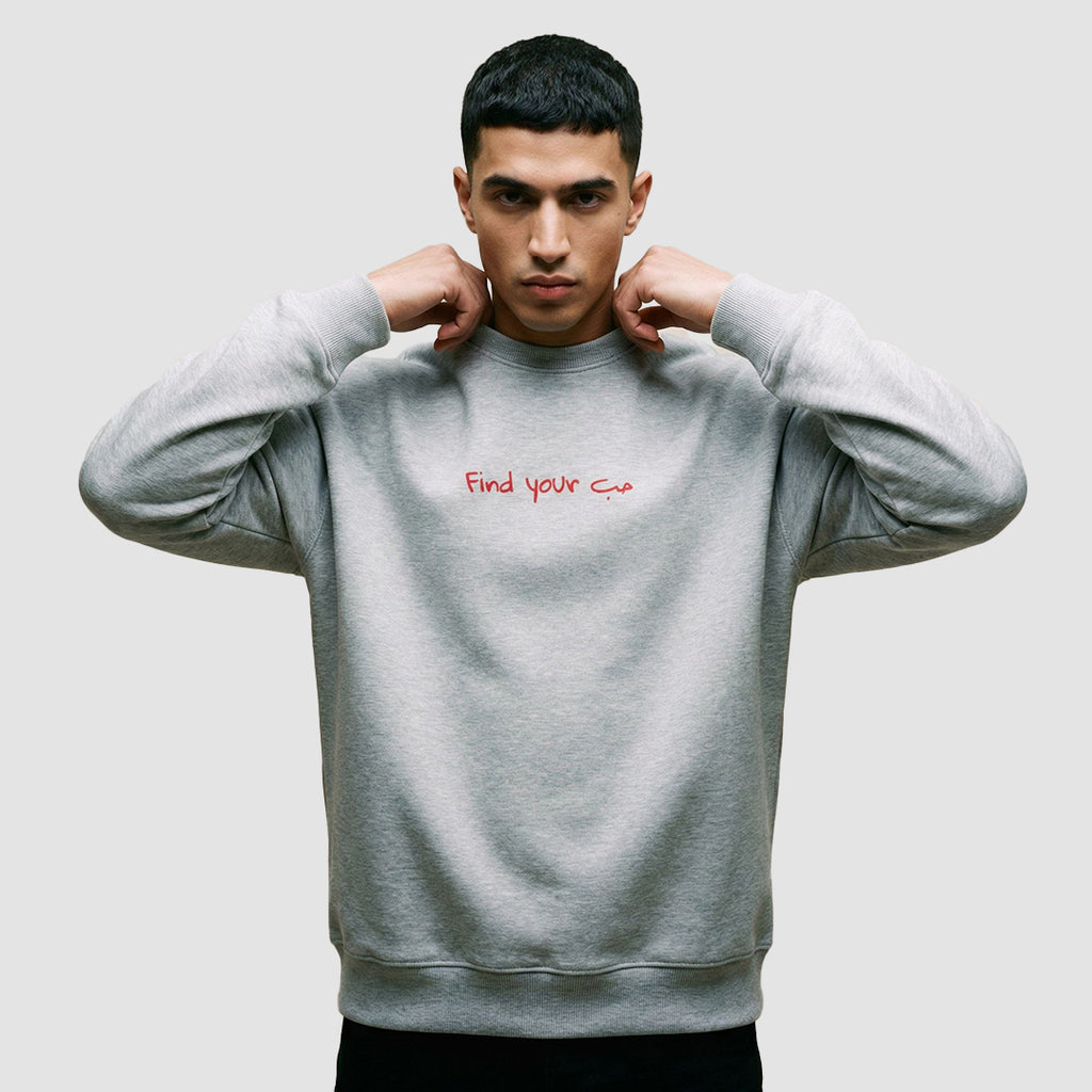 ragazzo indossa felpa unisex oversize grigia con scritta rossa in inglese e arabo find your love - Totally Random®