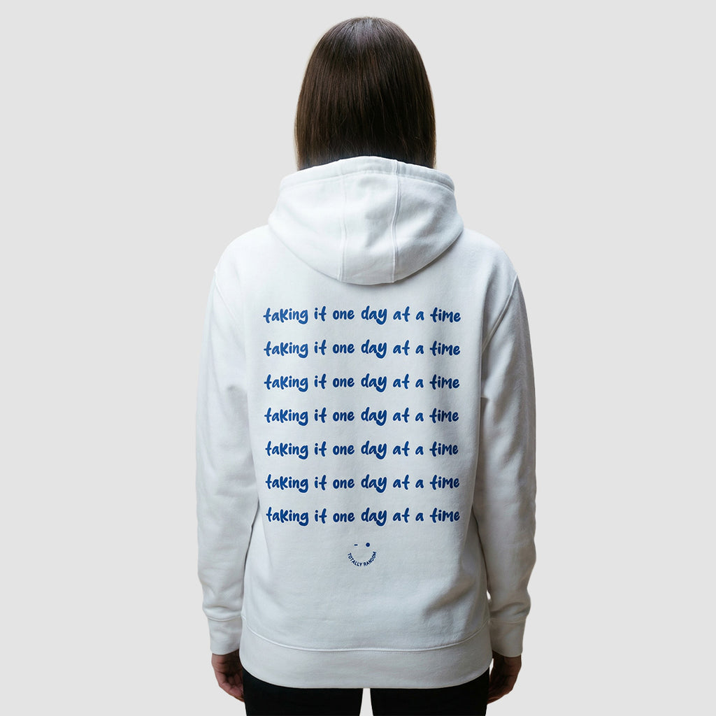 ragazza indossa felpa unisex bianca con cappuccio e scritta blu in inglese sulla schiena taking it one day at a time - Totally Random®